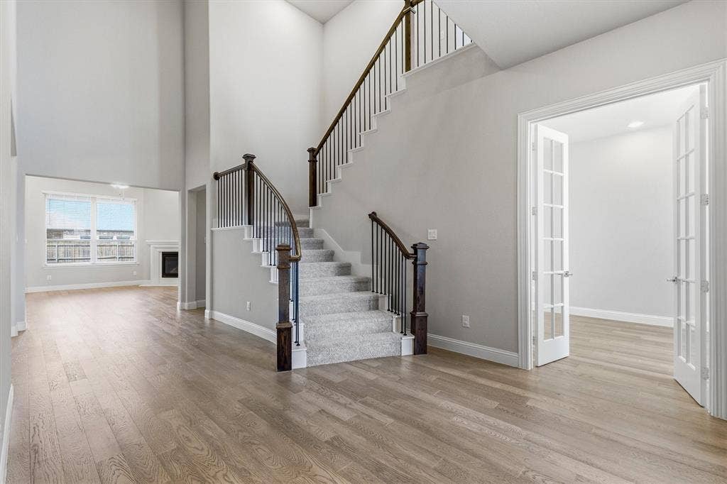 Two-story foyer with wood-finish flooring, a carpeted staircase with dark wood newel posts and metal balusters, and a room with French doors