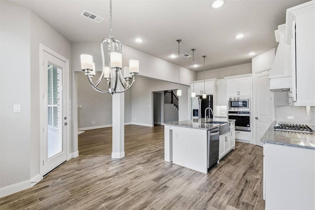 Kitchen featuring a large central island, stainless steel appliances, granite countertops, and wood-finish flooring