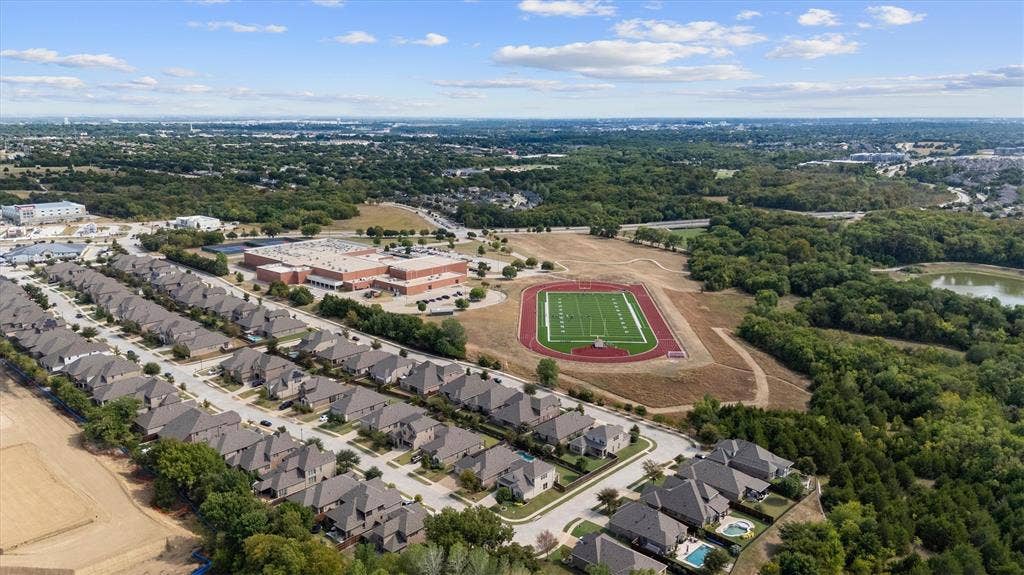 Aerial perspective highlighting a residential development with numerous detached homes, a sports field with a running track, and a large institutional building