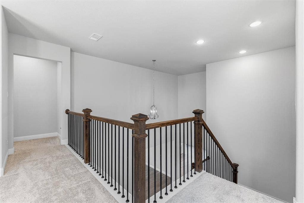 Carpeted landing featuring recessed lighting, a decorative chandelier, and a wood and iron staircase railing