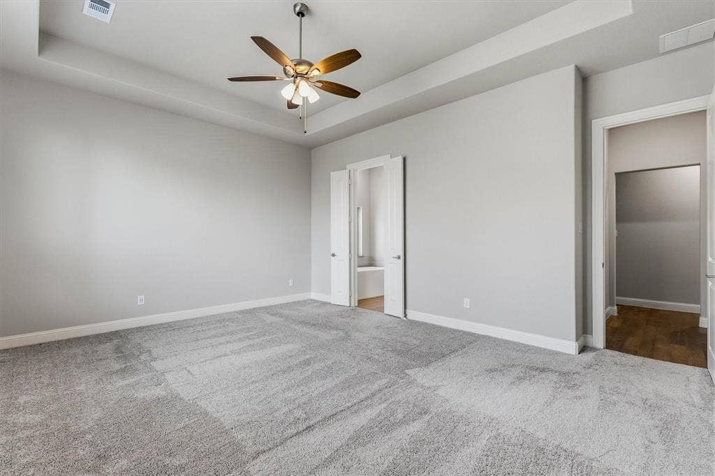Spacious room with tray ceiling, ceiling fan, neutral gray walls, and light gray carpet
