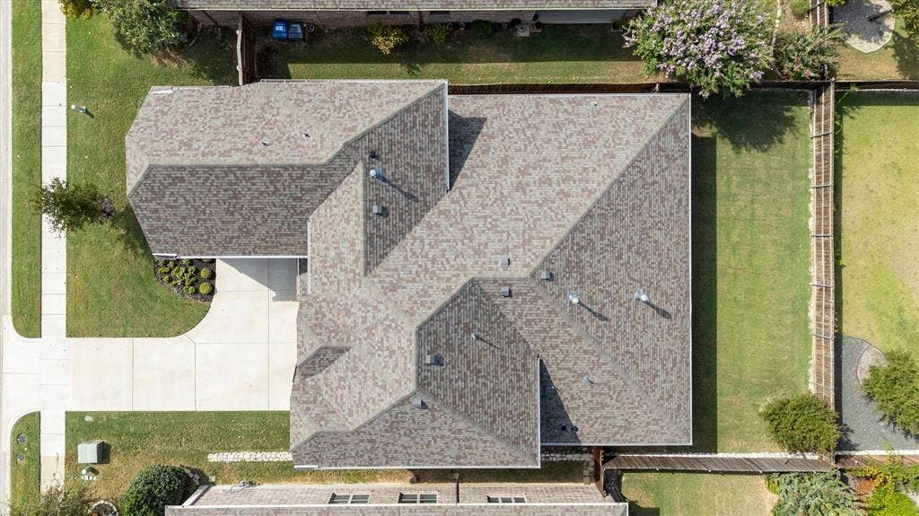 Asphalt shingle roof, concrete driveway, and manicured lawn