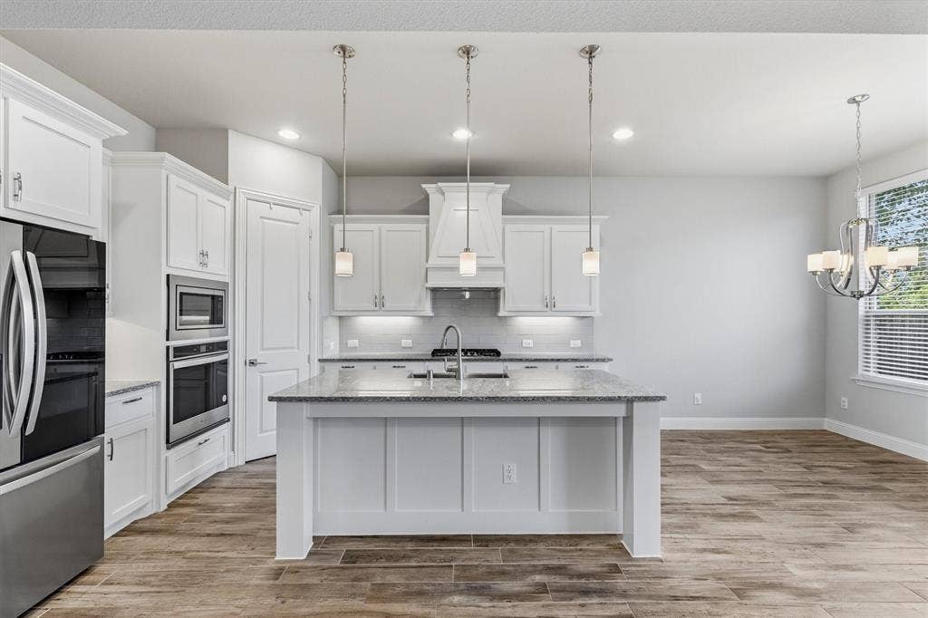 Kitchen featuring a central island with countertop, stainless steel appliances, pendant lighting, and wood-finish flooring