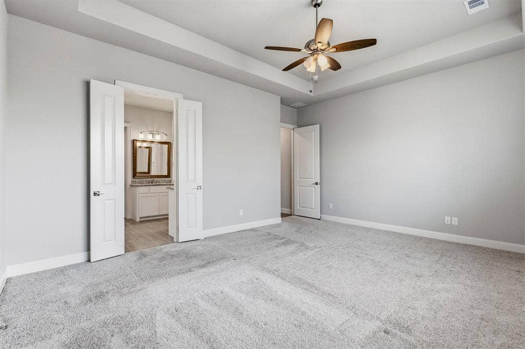 Tray ceiling with a ceiling fan, light gray wall paint, and gray carpeted flooring
