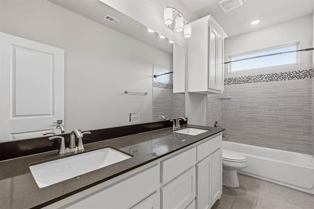 Dual vanity with undermount sinks, dark countertop, white cabinetry, integrated bathtub with tiled surround, and a clerestory window