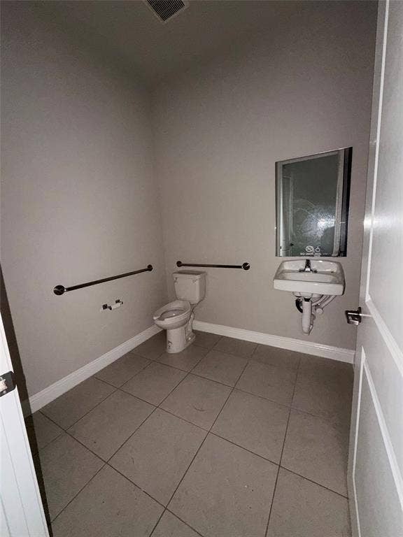 3721 S Stonebridge Drive, #704, McKinney, TX 75070 Tiled flooring, wall-mounted sink, toilet, built-in grab bars, and a white paneled door