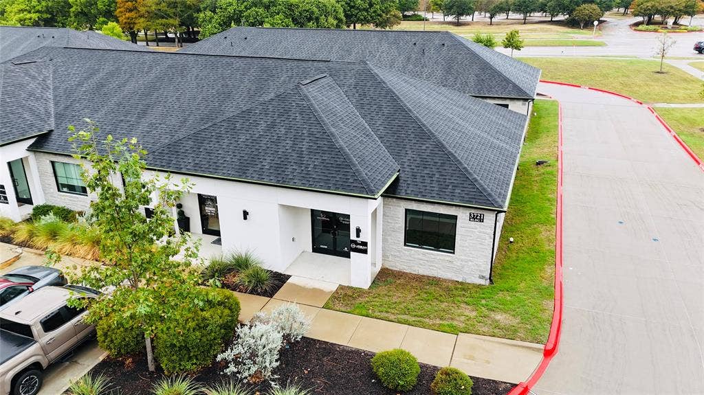 3721 S Stonebridge Drive, #704, McKinney, TX 75070 Modern commercial building featuring a dark shingle roof, white exterior with stone accents, and manicured landscaping