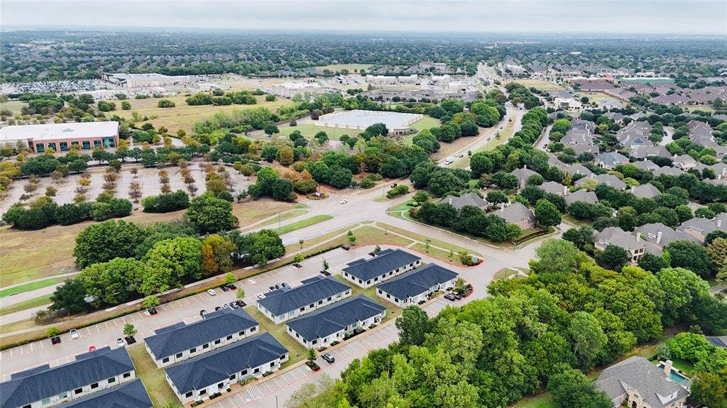 3721 S Stonebridge Drive, #704, McKinney, TX 75070 Aerial perspective showcasing commercial properties with dark roofs, surrounded by lush mature trees, and a residential area with varied rooflines