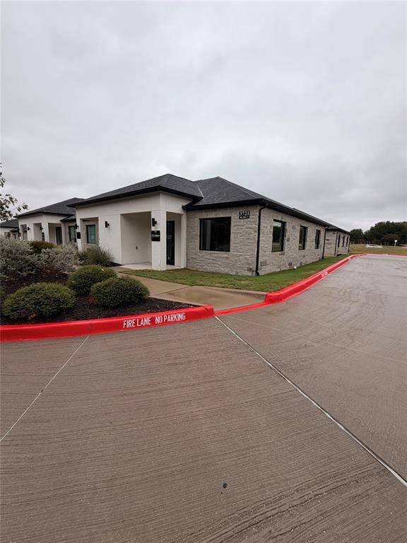 3721 S Stonebridge Drive, #704, McKinney, TX 75070 Building exterior featuring a black shingle roof, stone veneer, white stucco facade, and dark framed windows