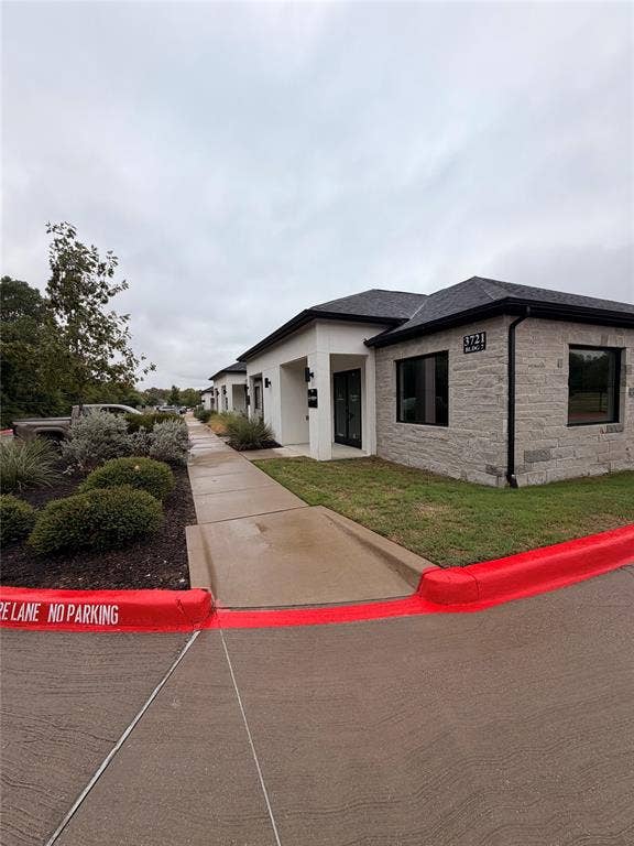 3721 S Stonebridge Drive, #704, McKinney, TX 75070 Stone facade building with a dark shingle roof, black-framed windows, and a paved walkway