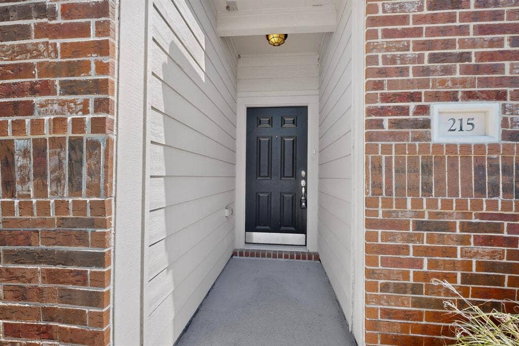 215 Magnolia Drive, Princeton, TX 75407 Brick and siding exterior with a paneled entry door, overhead lighting fixture, and visible address number