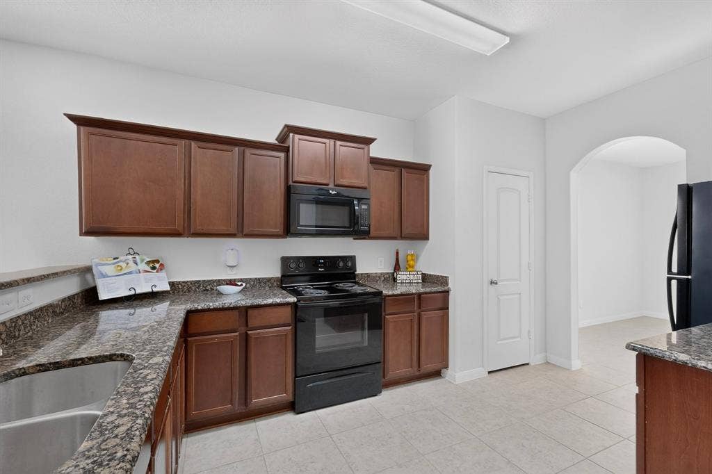 215 Magnolia Drive, Princeton, TX 75407 Kitchen featuring granite-style countertops, wood-finish cabinetry, stainless steel sink, and tile flooring