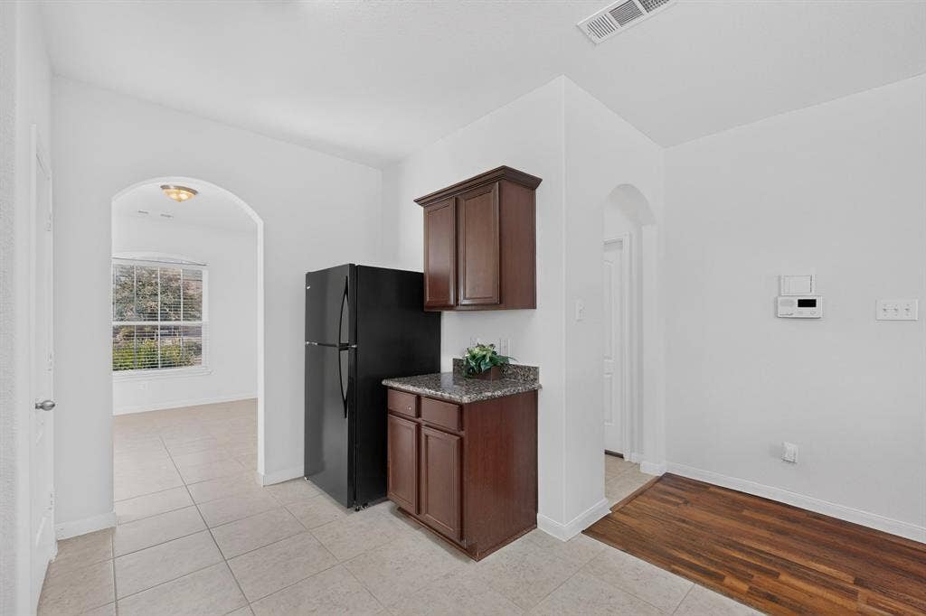 215 Magnolia Drive, Princeton, TX 75407 Arched doorway, tile flooring, wood-finish flooring, dark wood cabinetry, and a granite-finish countertop