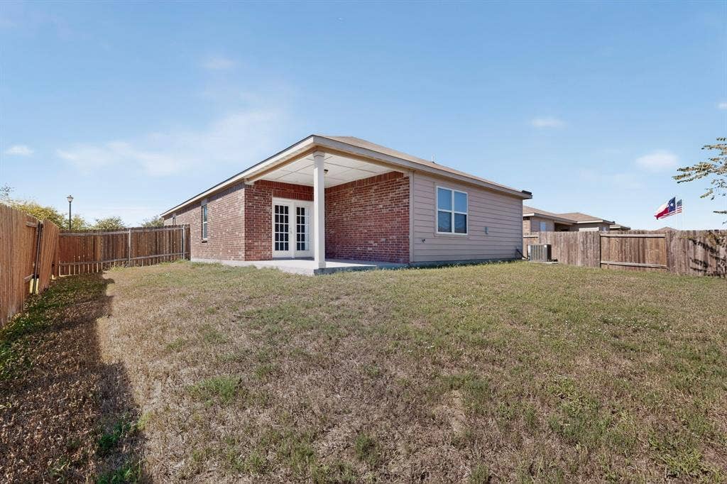 215 Magnolia Drive, Princeton, TX 75407 Brick and siding exterior with a covered patio, double-pane windows, and a wood privacy fence