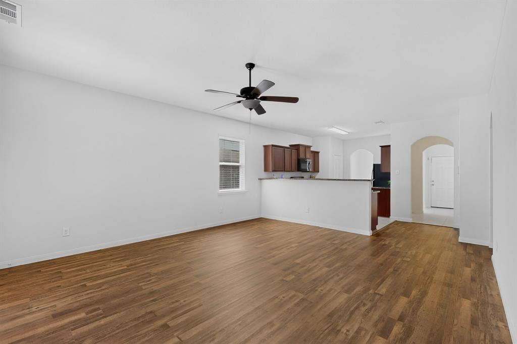 215 Magnolia Drive, Princeton, TX 75407 Spacious living area with wood-finish flooring, a ceiling fan, and a pass-through to the kitchen featuring dark wood cabinetry and a breakfast bar