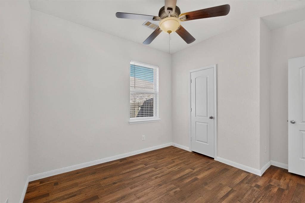 215 Magnolia Drive, Princeton, TX 75407 Light-filled room featuring wood-finish flooring, a white window with blinds, a ceiling fan with light fixture, and two white panel doors