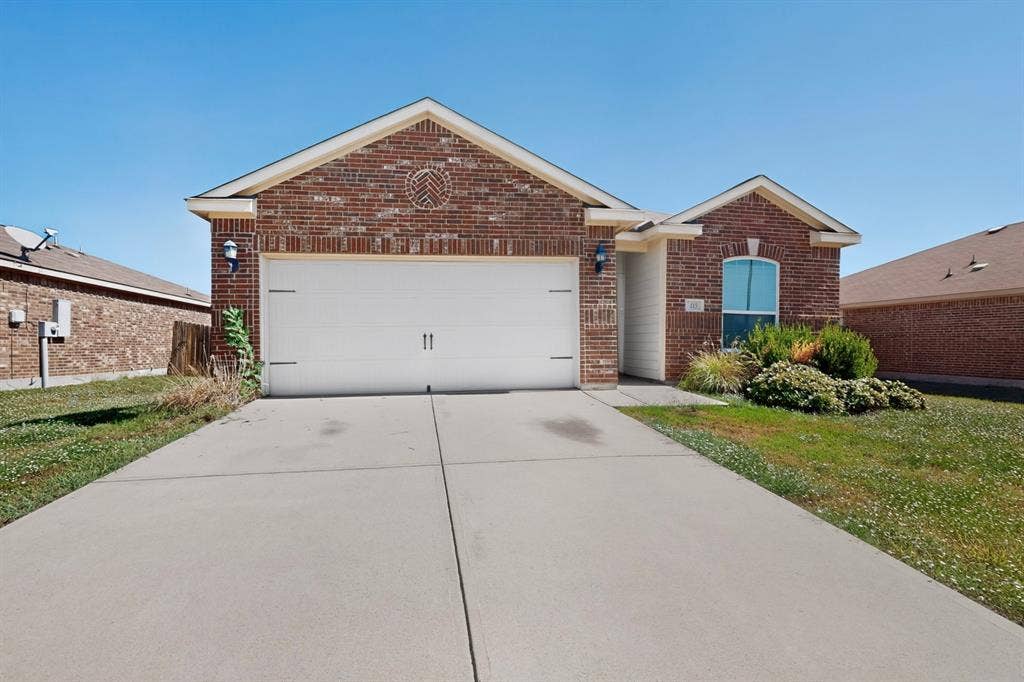 215 Magnolia Drive, Princeton, TX 75407 Welcoming brick exterior with a white two-car garage door, complemented by manicured landscaping and a concrete driveway