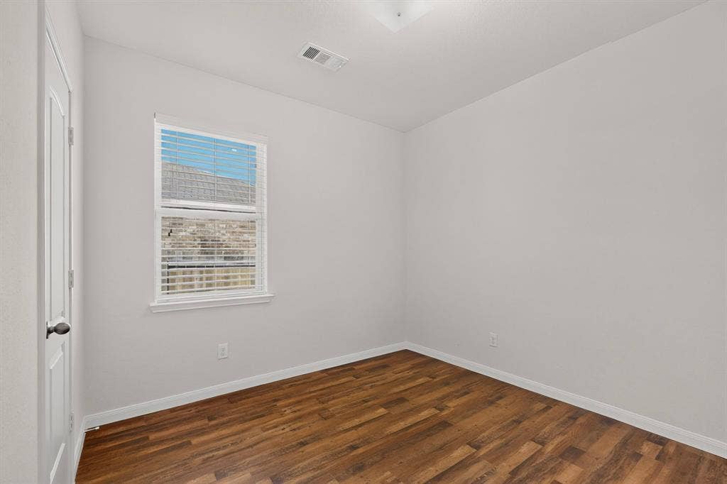 215 Magnolia Drive, Princeton, TX 75407 Wood-finish flooring with white baseboards, a single window with blinds, and a white interior door with a black knob