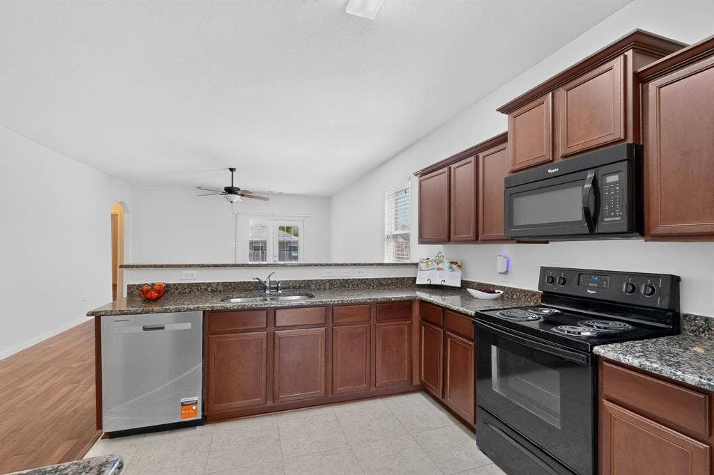 215 Magnolia Drive, Princeton, TX 75407 Kitchen featuring wood-finish cabinetry, granite countertops, tile flooring, and integrated black appliances