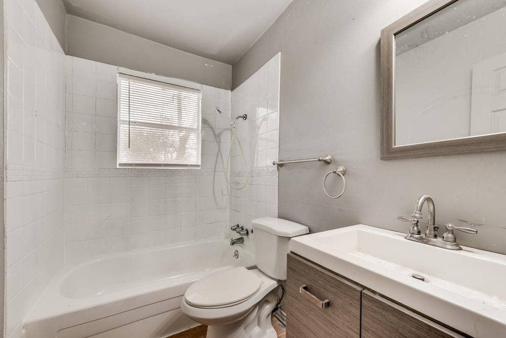 4414 Cinda Ree Lane, Dallas, TX 75216 White tiled shower/tub combination with a window, modern vanity with wood-finish cabinetry, and a framed mirror