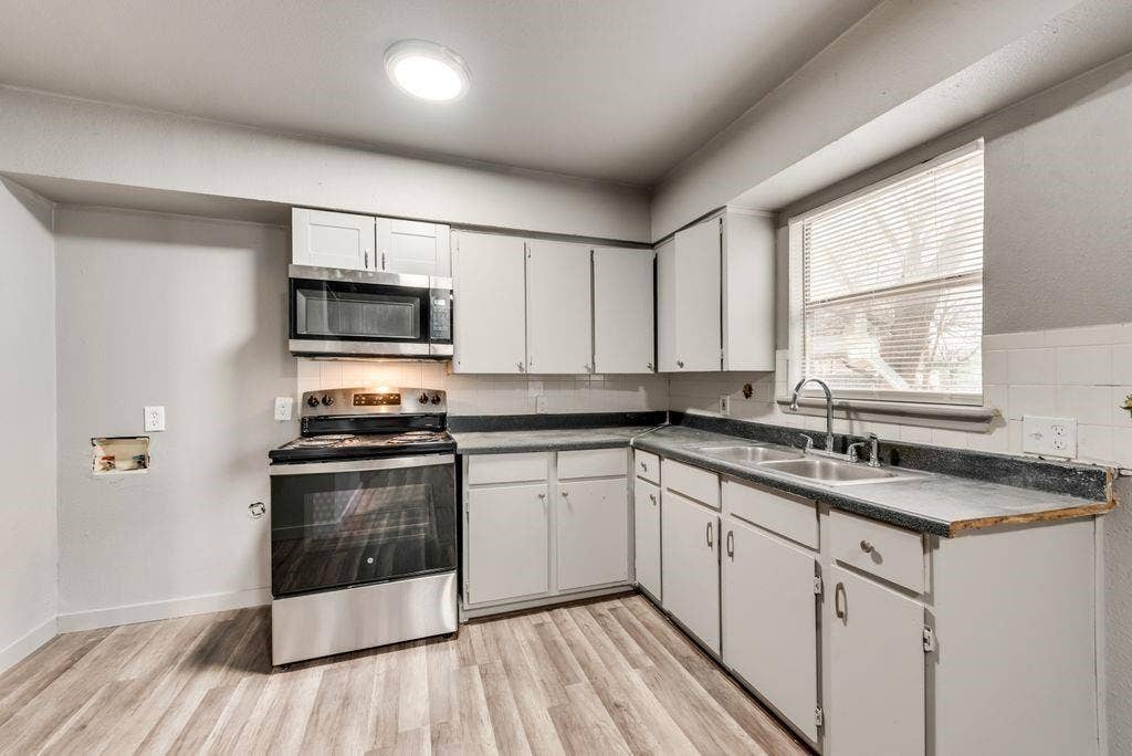 4414 Cinda Ree Lane, Dallas, TX 75216 Kitchen featuring wood-finish flooring, white cabinetry, stainless steel appliances, a dual basin sink, and a window