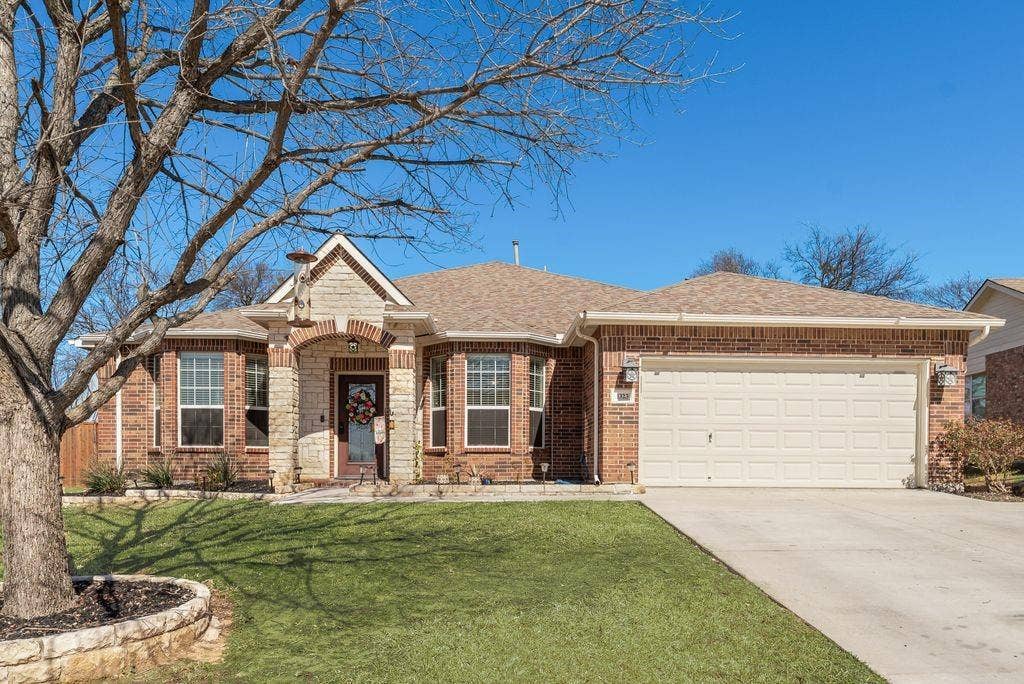 1323 Canyon Creek Road, Wylie, TX 75098 Charming brick residence featuring a welcoming front elevation with arched entry, multi-pane windows, and stone accents