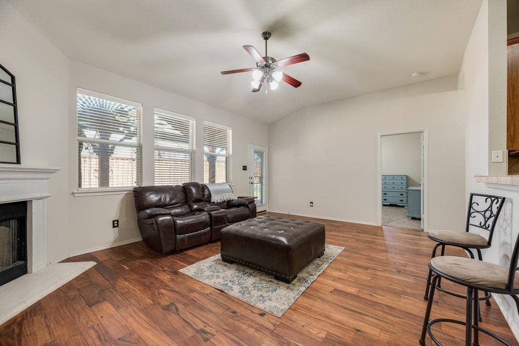 1323 Canyon Creek Road, Wylie, TX 75098 Vaulted ceiling living area featuring wood-finish flooring, a white mantel, and a multi-blade ceiling fan