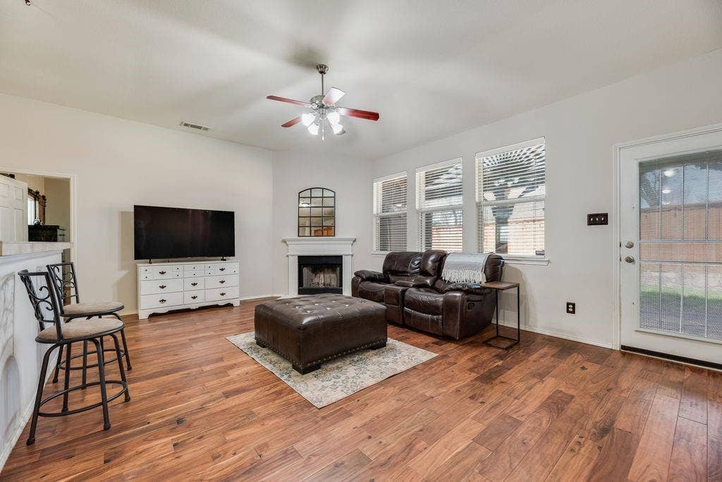1323 Canyon Creek Road, Wylie, TX 75098 Wood-finish flooring throughout, vaulted ceiling, ceiling fan, white paneled fireplace, and multiple windows with blinds