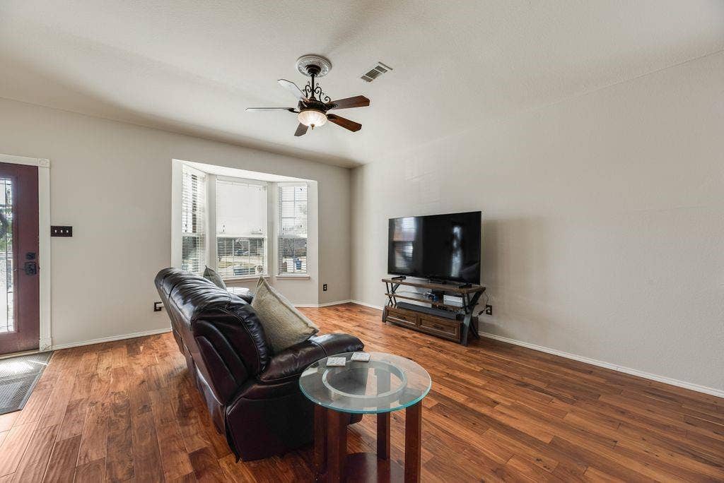 1323 Canyon Creek Road, Wylie, TX 75098 Wood-finish flooring throughout, bay window with blinds, ceiling fan, and a red-finish entry door with decorative glass