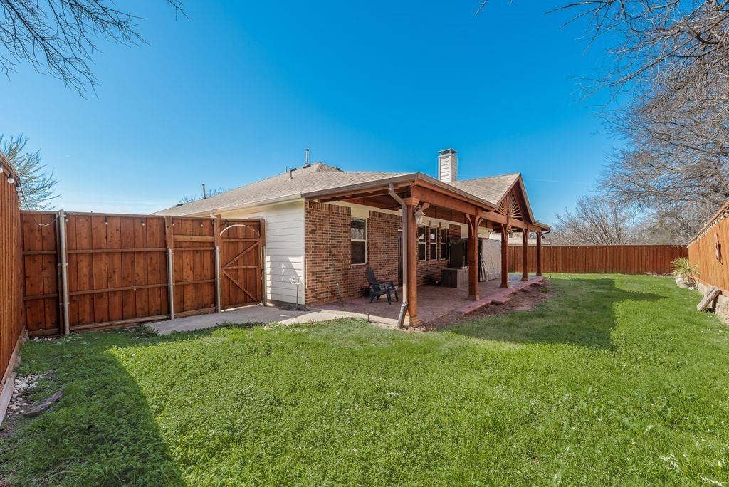 1323 Canyon Creek Road, Wylie, TX 75098 Expansive backyard featuring a covered patio, privacy fencing, and a brick exterior with white siding