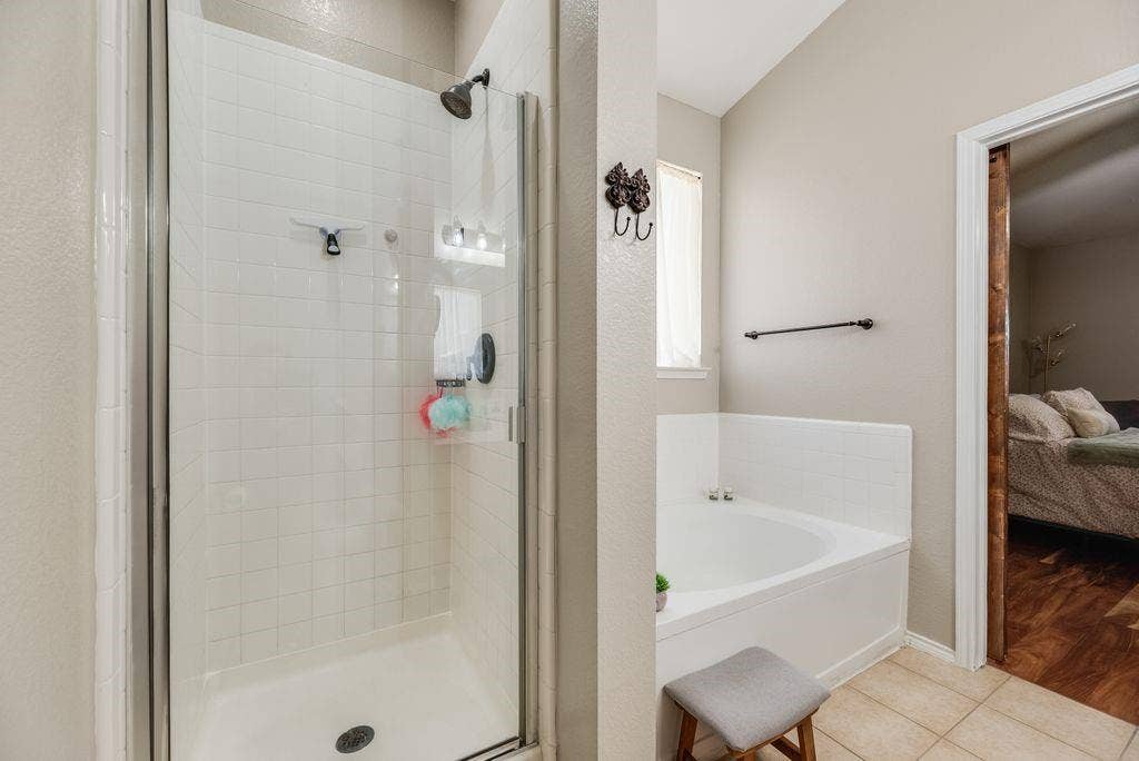 1323 Canyon Creek Road, Wylie, TX 75098 White tiled shower with glass enclosure, corner soaking tub, and neutral-toned wall paint