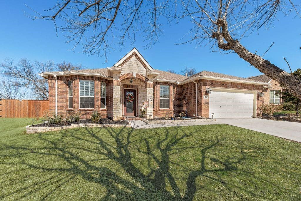 1323 Canyon Creek Road, Wylie, TX 75098 Brick and stone facade with an arched entry, two-car garage, concrete driveway, and a wood privacy fence