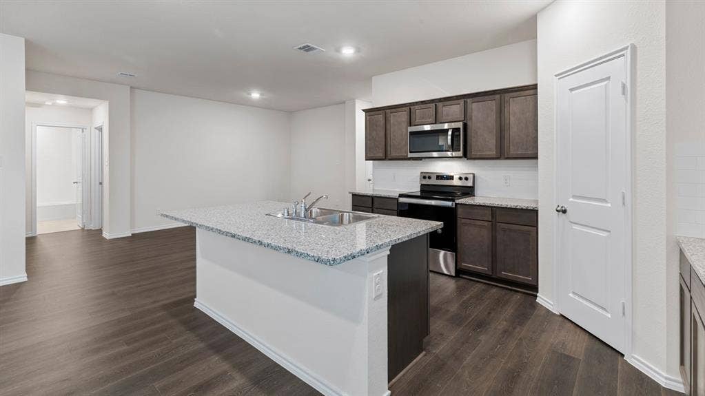 5012 Shumard Drive, Lindale, TX 75771 Kitchen featuring an island with a dual-basin sink, dark wood-finish cabinetry, stainless steel appliances, and wood-finish flooring