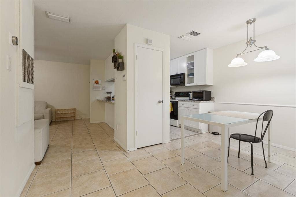 5981 Arapaho Road, #103, Dallas, TX 75248 Kitchen featuring white cabinetry with upper glass-front display cabinets, black appliances, and a dining area with a two-light pendant fixture