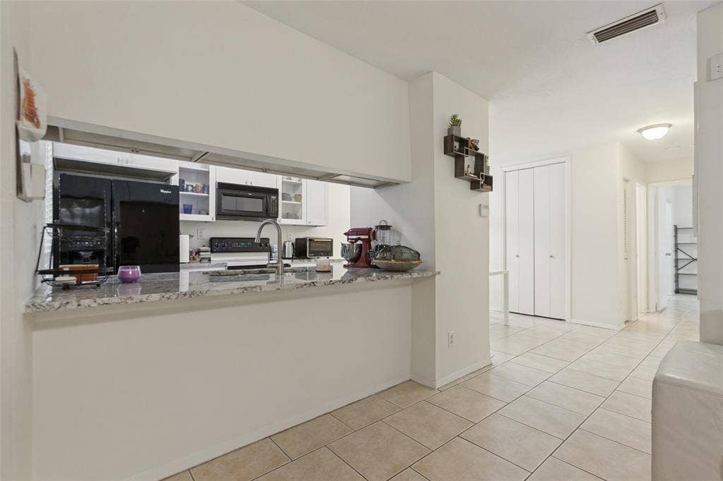 5981 Arapaho Road, #103, Dallas, TX 75248 Kitchen pass-through with a stone-finish countertop, white cabinetry, and stainless-steel finish faucet