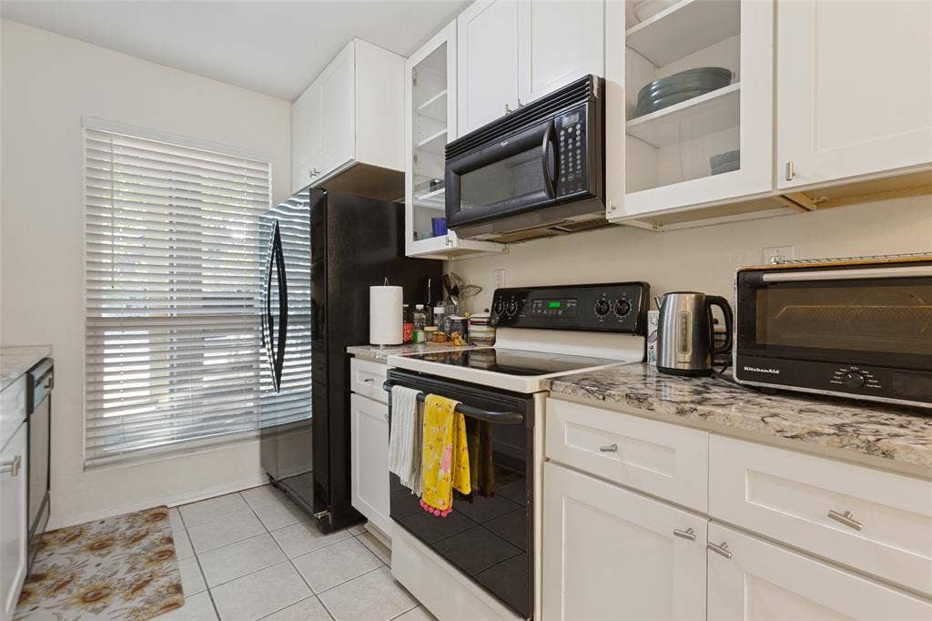 5981 Arapaho Road, #103, Dallas, TX 75248 White shaker-style cabinetry with varied glass-front upper cabinets, light-toned countertops, and a full suite of black appliances