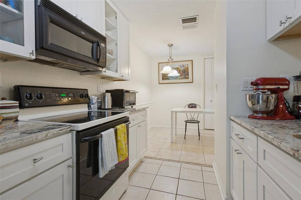 5981 Arapaho Road, #103, Dallas, TX 75248 White cabinetry with brushed nickel hardware, light-toned stone-finish countertops, black built-in microwave, black electric range, and light-toned floor tiling
