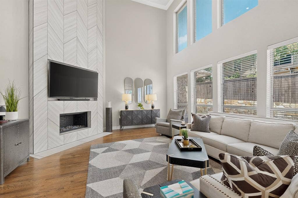 1494 Willingham Drive, Allen, TX 75013 Two-story living room featuring a herringbone-patterned fireplace with an integrated linear firebox, natural wood-finish flooring, and expansive windows