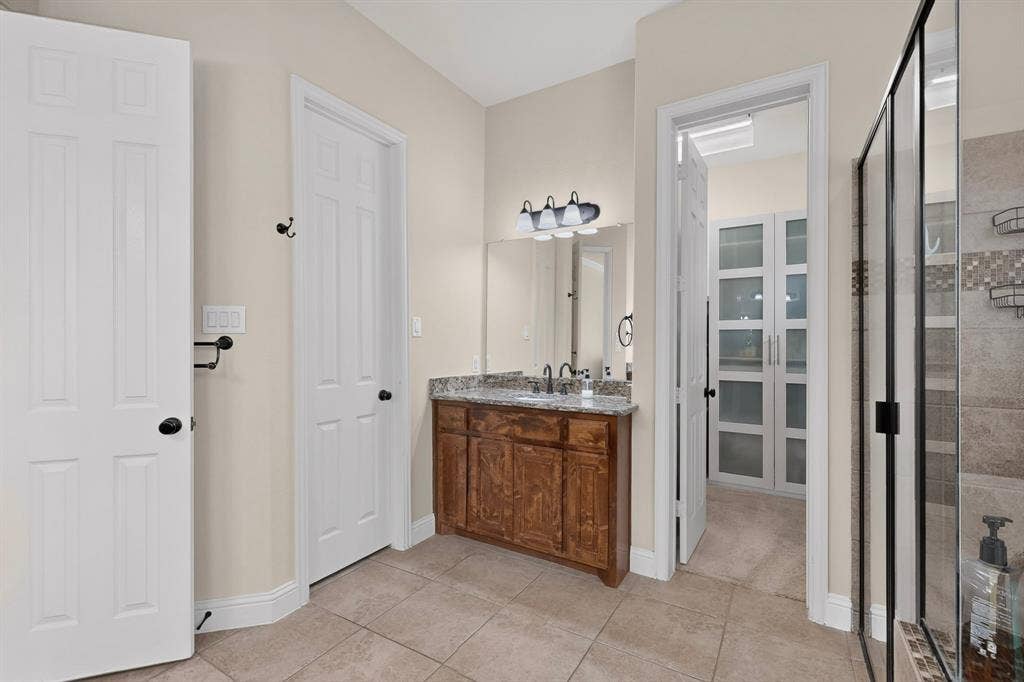 1494 Willingham Drive, Allen, TX 75013 Wood-finish vanity with a stone countertop, tile flooring, and a glass-enclosed shower with tiled walls