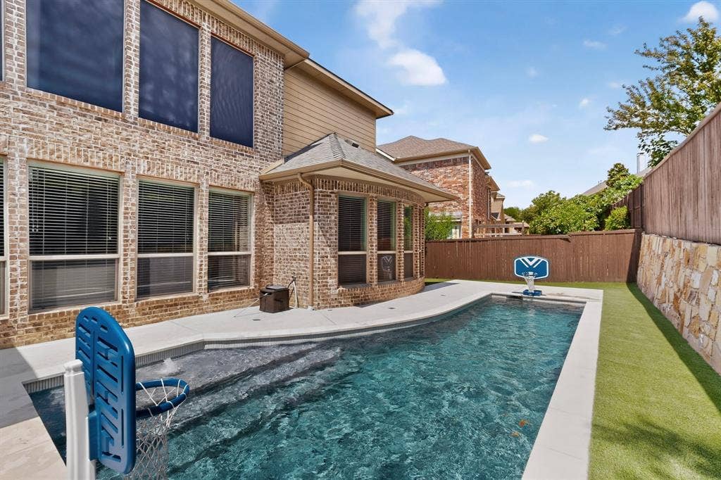 1494 Willingham Drive, Allen, TX 75013 Brick exterior with multiple windows, inground pool with integrated steps, artificial turf area, and a stone retaining wall