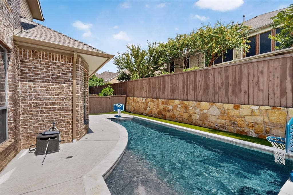 1494 Willingham Drive, Allen, TX 75013 Brick exterior, curved concrete patio, in-ground swimming pool, stone retaining wall, and wood privacy fencing