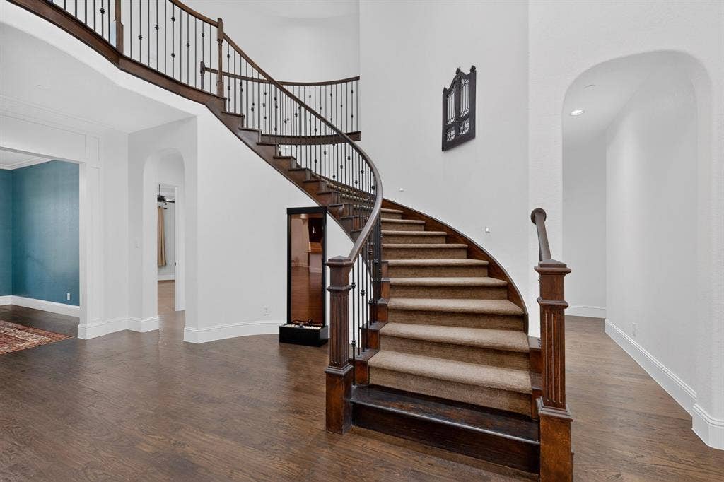 13853 Myatt Avenue, Frisco, TX 75035 Grand curved staircase with dark wood-finish treads and risers, complemented by a wrought iron balustrade