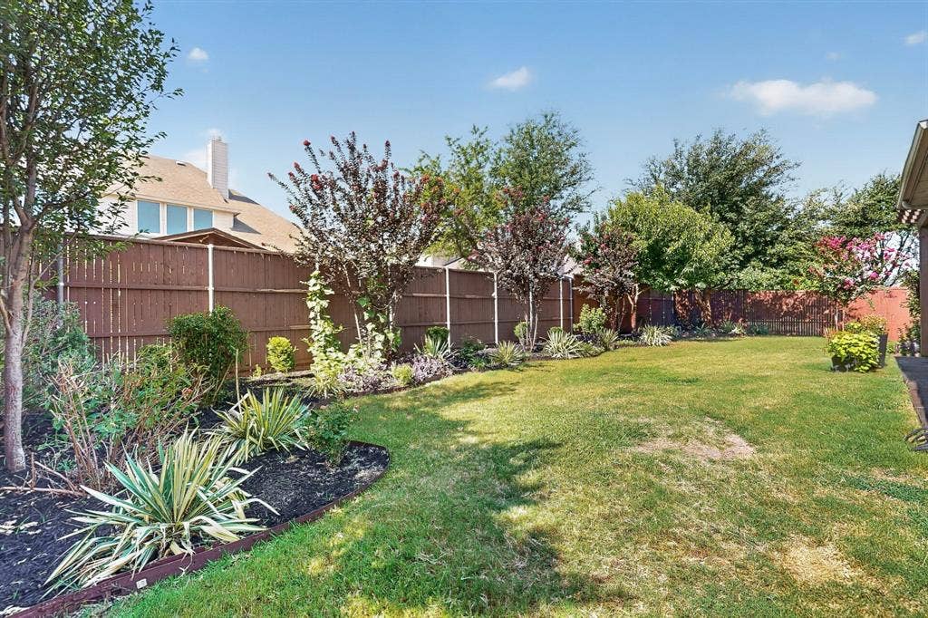13853 Myatt Avenue, Frisco, TX 75035 Spacious backyard with a vibrant green lawn, featuring mature trees and established landscaping beds