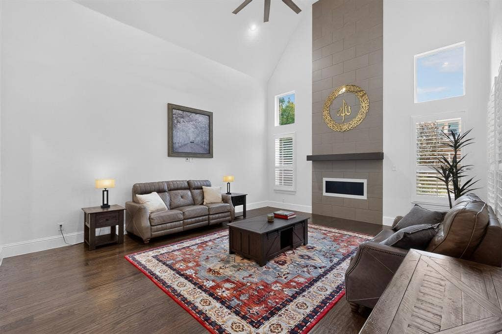 13853 Myatt Avenue, Frisco, TX 75035 Living area featuring vaulted ceilings, wood-finish flooring, a contemporary fireplace with a stone surround, and multiple windows with plantation shutters