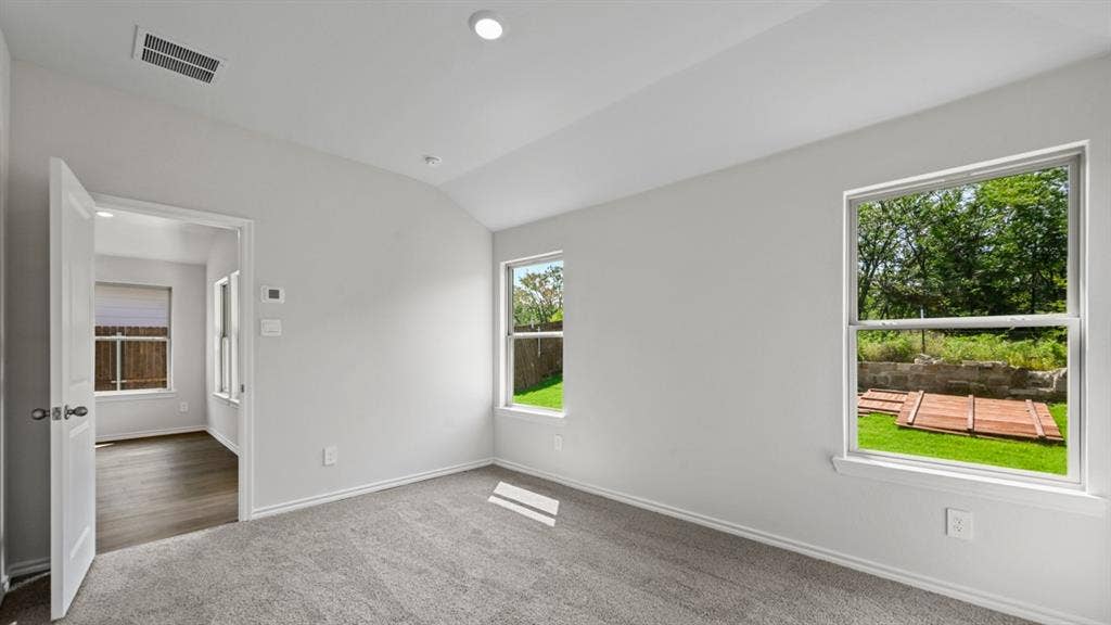 1667 Blaire Drive, Tyler, TX 75702 Carpeted room featuring two windows with outdoor views, light gray walls, and an open doorway leading to a room with wood-finish flooring