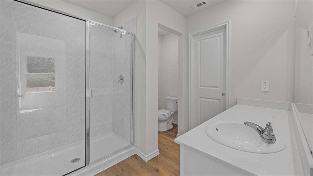 1667 Blaire Drive, Tyler, TX 75702 Modern bathroom featuring a glass-enclosed shower with white tiled walls, a white vanity with an integrated sink, chrome fixtures, and wood-finish flooring