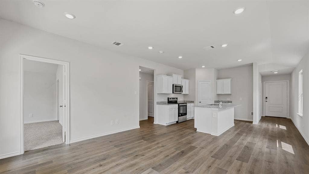 1667 Blaire Drive, Tyler, TX 75702 Open-concept living area featuring wood-finish flooring, recessed lighting, and a kitchen with white cabinetry, stainless steel appliances, and an island with a light-toned countertop