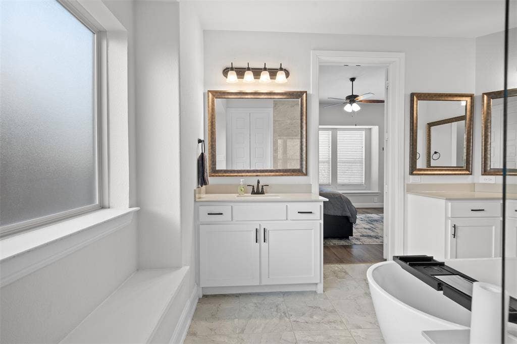 Frosted window, built-in window bench, white vanity with countertop, framed mirror, and freestanding bathtub