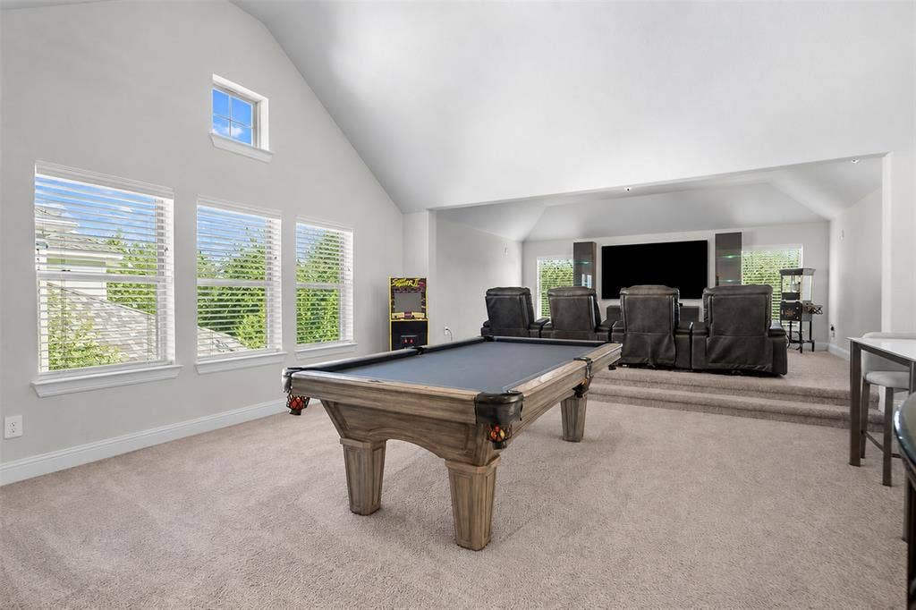Vaulted ceiling, multiple windows with blinds, carpeted flooring, elevated media area, and a built-in bar table