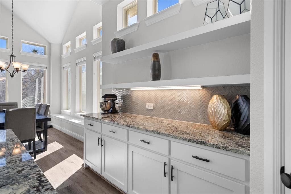 White shaker-style cabinetry with matte black hardware, stone-finish countertops, and under-cabinet lighting
